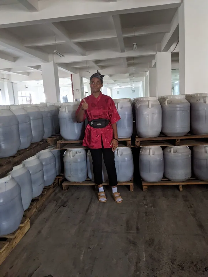 Cynthia giving a thumbs-up among stacked storage drums during a company visit in China