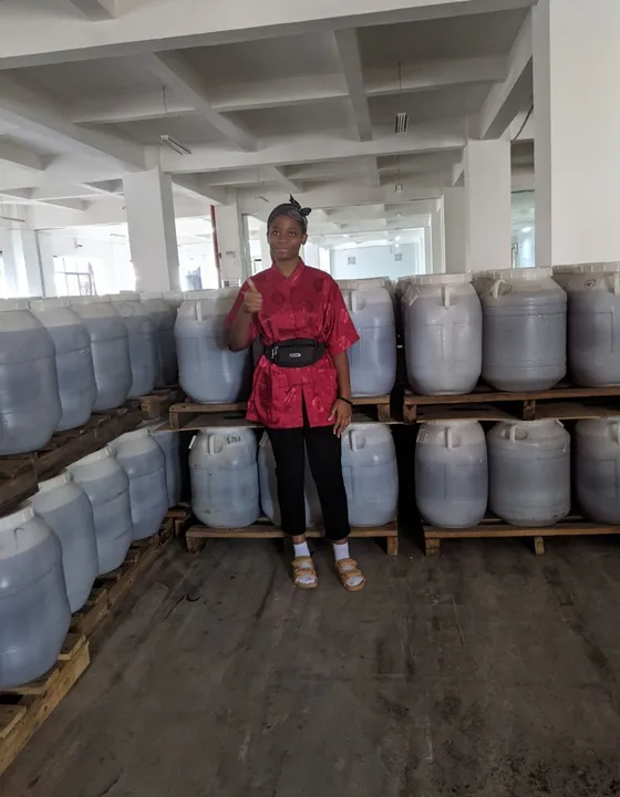 Cynthia giving a thumbs-up among stacked storage drums during a company visit in China