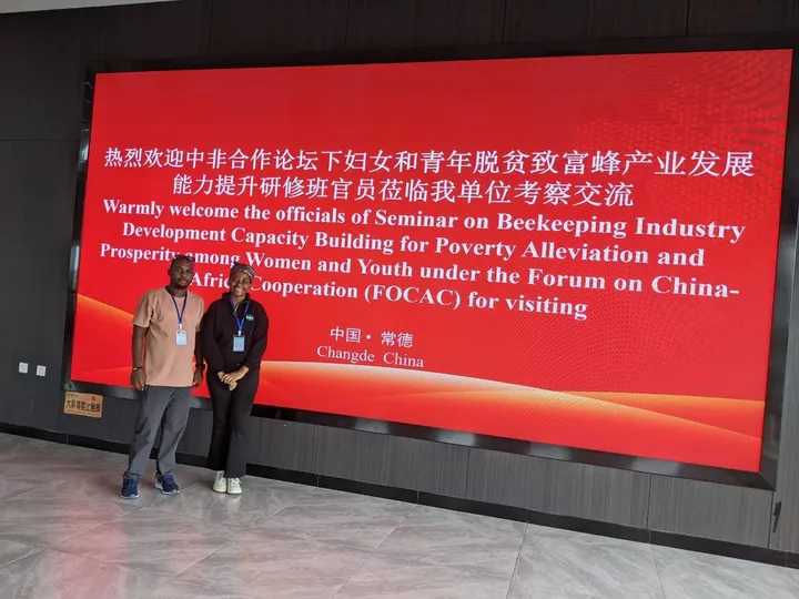 Two team members in front of the FOCAC beekeeping seminar welcome screen in Changde, China